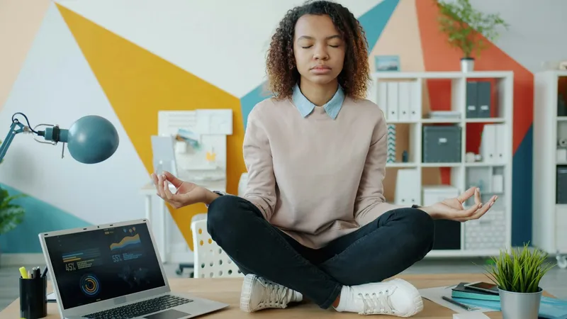 Henkilö meditoi toimiston pöydällä kannettavan tietokoneen vieressä