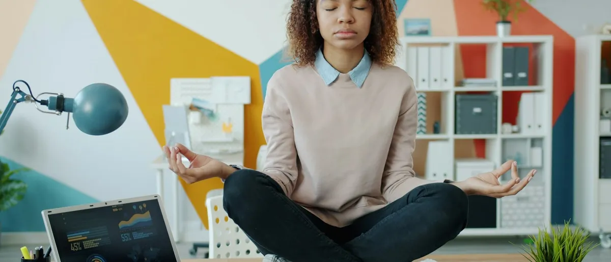Henkilö meditoi toimiston pöydällä kannettavan tietokoneen vieressä