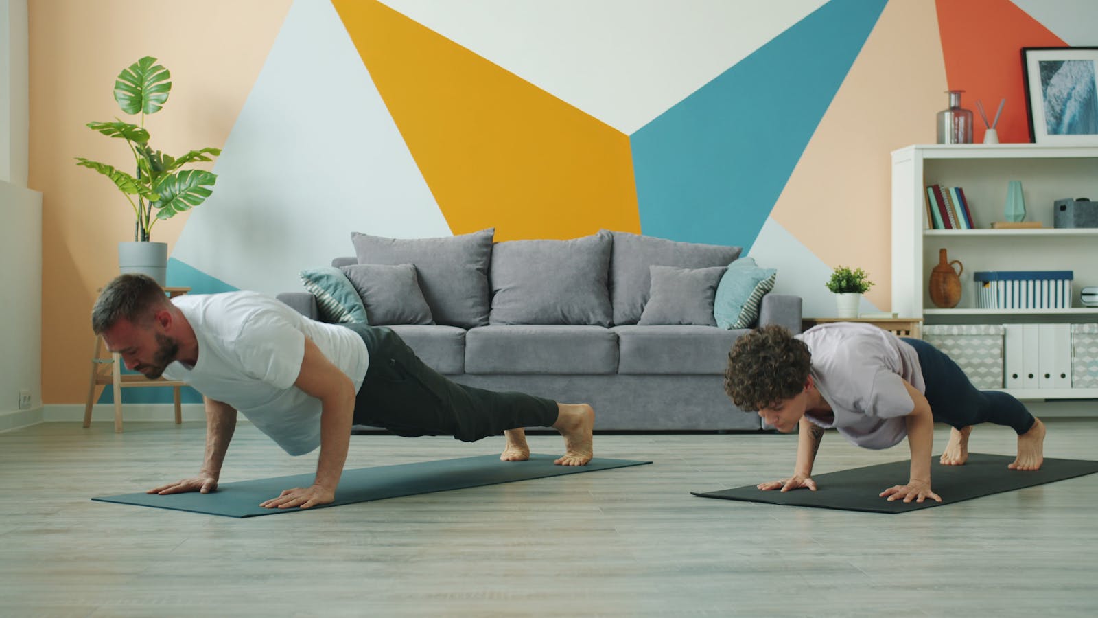 Two people doing push-ups on exercise mats in a bright living room