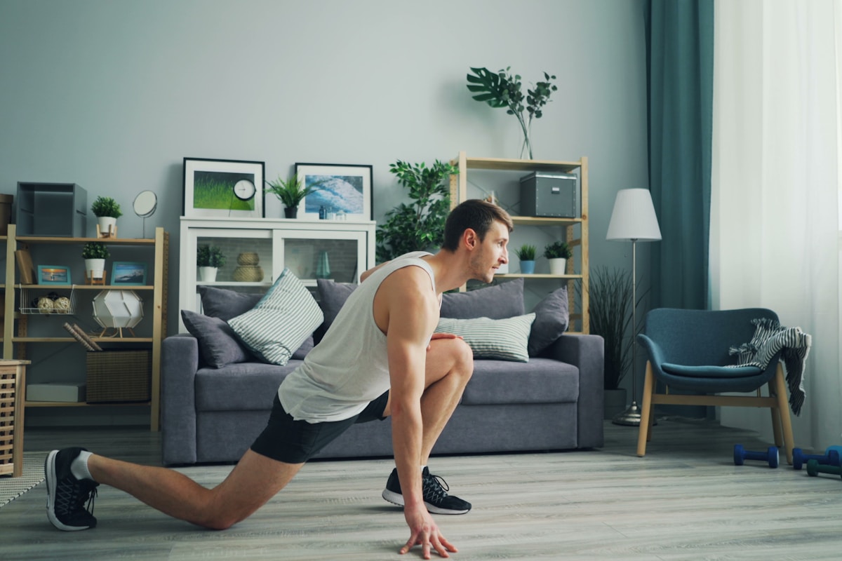Man performing a bodyweight lunge in his living room, demonstrating progressive overload training with no gym equipment