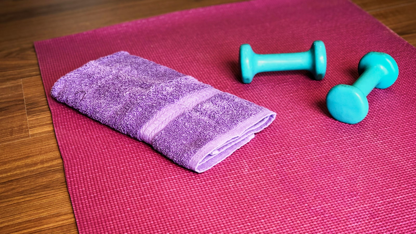Yogamatte mit kleinen Hanteln und gefaltetem Handtuch bereit für ein Heimtraining