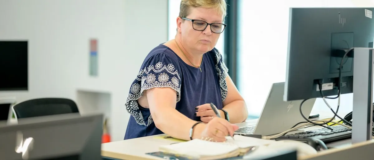 Büromitarbeiterin an einem Stehschreibtisch macht sich neben einem Laptop Notizen