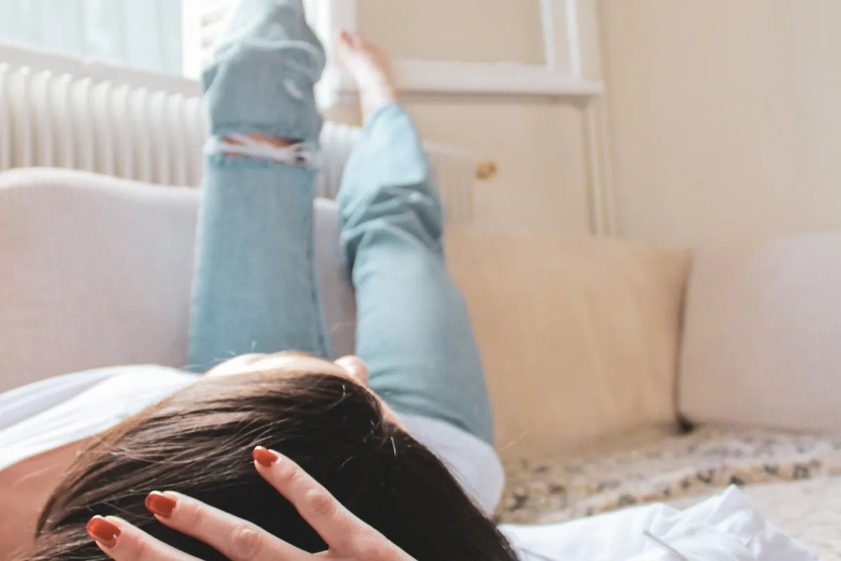 Woman resting with legs elevated on a couch, representing sleep and recovery as the foundation of athletic performance