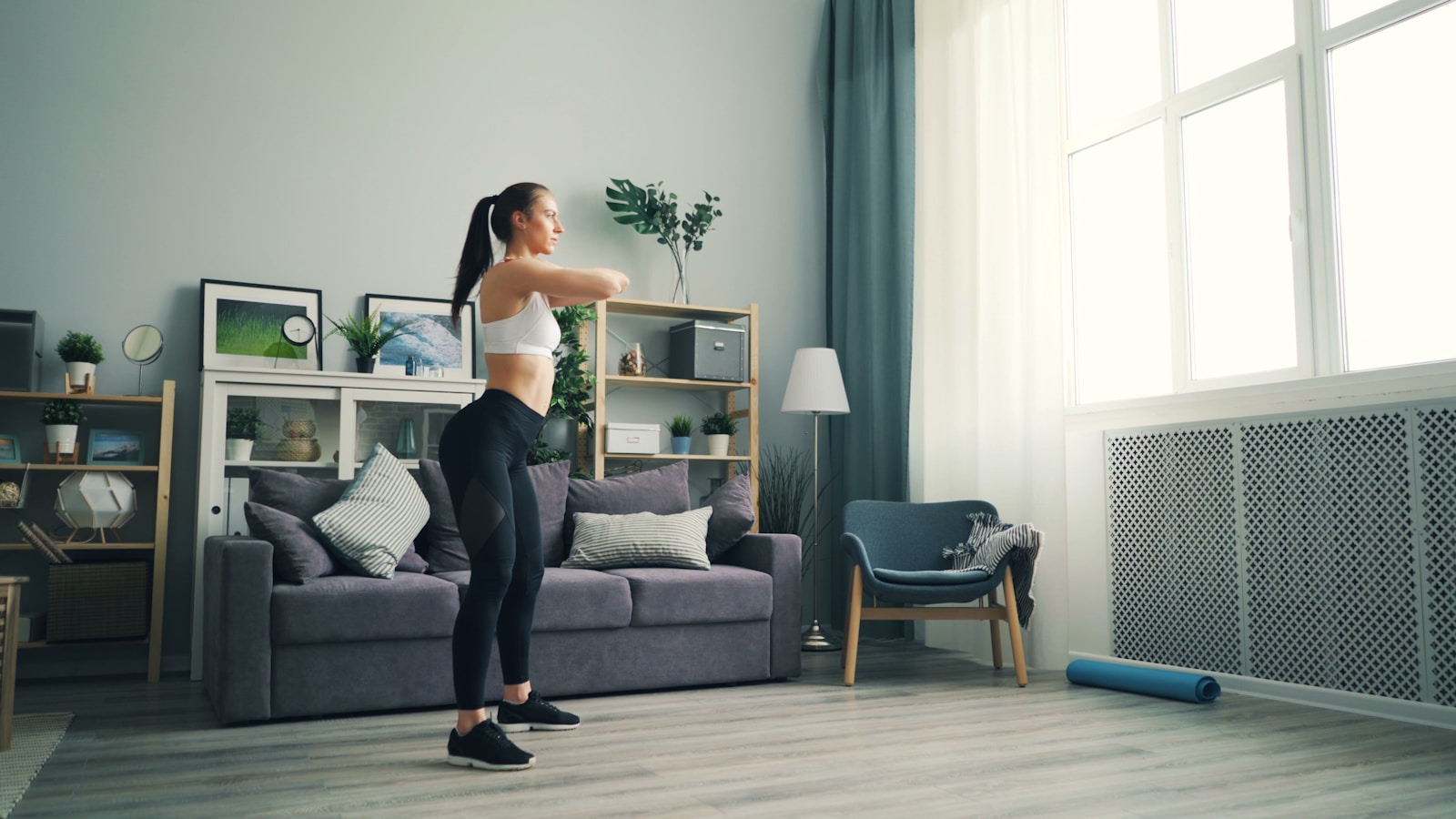Frau macht ein Workout im Stehen in einem hellen Wohnzimmer
