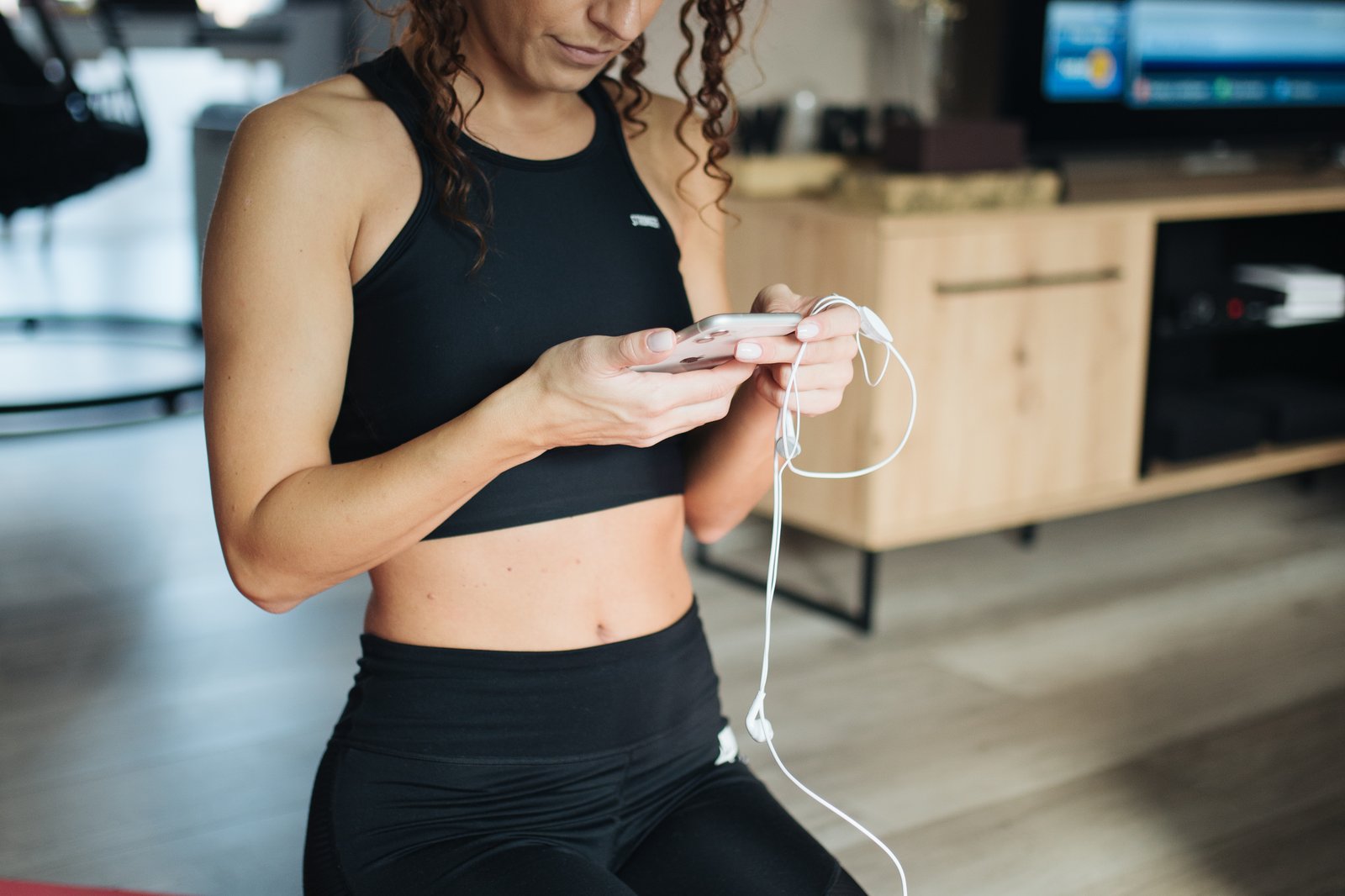 Person checking fitness app on smartphone while sitting on a yoga mat in a home setting