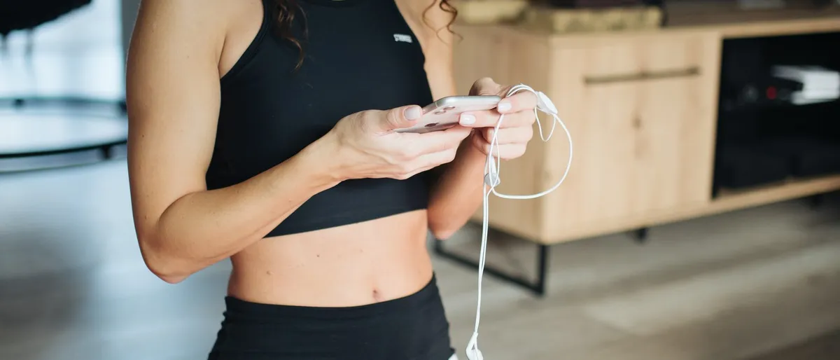 Persona che controlla un app fitness su smartphone seduta su un tappetino yoga in un ambiente domestico